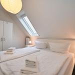 Schlafzimmer mit Dachschrägen, Bett, Nachttisch, Kleiderschrank und Dachfenster.