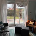 Wohnzimmer mit Sofa, Sessel und Blick auf Garten durch Glastür
