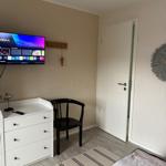 Schlafzimmer mit Bett, TV, Schrank und Stuhl. Tür und Wandverkleidung sind sichtbar.