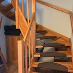 Holztreppe mit Teppichstufen und Geländer führt nach oben.