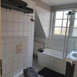 Badezimmer mit Badewanne, Toilette und Waschbecken. Weiße Fliesen und Fenster mit Blick.