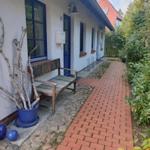 Haus mit blauer Tür, Stein- und Ziegelweg, Bank und Pflanzen im Vorgarten.