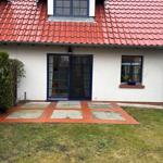 Haus mit rotem Dach, blauen Fenstern und gepflastertem Vorgarten.