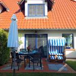 Terrasse mit Tisch, Stühlen und Strandkörben unter blau-weißem Zelt.