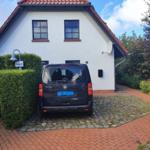 Ein Haus mit rotem Dach und weißer Fassade. Ein schwarzes Auto steht auf einem Kiesplatz.