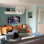 Wohnzimmer mit Sofa, Sesseln, Fernseher und Deckenleuchte.