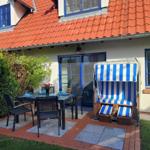 Terrasse mit Tisch, Stühlen und Strandkorb. Haus mit rotem Dach und blauen Fenstern.