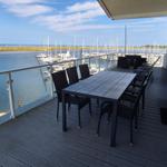 Terrasse mit Tisch und Stühlen, Blick auf Hafen mit Segelyachten.