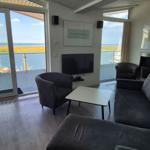 Wohnzimmer mit Sofa, Sessel und TV. Große Fenster mit Blick auf Hafen und Wasser.