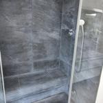 Dusche mit Glaswand, dunklen Fliesen und zwei Duschköpfen an der Decke.