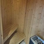 Sauna mit Holzwand und Sitzbank, daneben Heizgerät mit Steinen.