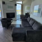 Wohnzimmer mit Sofa, Sessel und TV. Balkon mit Blick auf Wasser und Schiffe.