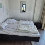 Schlafzimmer mit Doppelbett, Spiegel und Fensterblick auf Grünfläche.