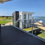 Terrasse mit Blick auf Wasser, Bootshäfen und grüne Landschaft.