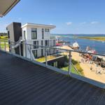 Terrasse mit Blick auf Hafen und Wasser. Moderne Gebäude und Boote sind sichtbar.