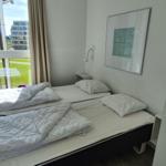 Zimmer mit zwei Einzelbetten, Fenster mit Blick auf Grünfläche und Gebäude.