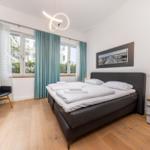 Schlafzimmer mit Bett, Nachttisch und Fenster mit Vorhängen.