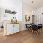 Essbereich mit Tisch, Stühlen und Glasvitrine. Küchenbereich mit Dunstabzug.