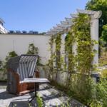 Terrasse mit Liegestuhl, Tisch und Pergola. Hinterhof mit grüner Umgebung und Steinweg.
