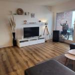 Wohnzimmer mit Fernseher, Holzboden und Balkonzugang.