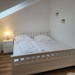 Schlafzimmer mit weißem Bett, Nachttisch und Lampe unter Dachschräge.