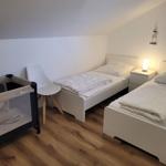 Zwei Einzelbetten, ein Kinderbett und eine Stehlampe in einem Schlafzimmer mit Holzboden.