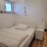Schlafzimmer mit Bett, Nachttisch und Fenster. An der Wand hängt ein Anker.