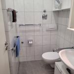 Badezimmer mit Toilette, Waschbecken und Handtuchhaltern. Fliesenwand und grauer Boden.