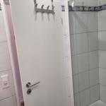 Dusche mit Glaswand, weiße Tür mit Haken und Fliesen mit Mosaikverzierung.