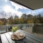 Terrasse mit Tisch, Pflanze und Laterne. Blick auf Bäume und Himmel.
