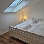 Schlafzimmer mit Dachfenster, weißem Bett und Nachttisch mit Lampe.