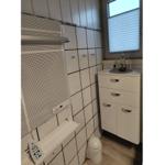 Badezimmer mit weißen Fliesen, Schrank und Fenster mit Jalousie.