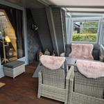Terrasse mit Rattanmöbeln, rosa Felldecken und Holzboden. Durchgang ins Innere.