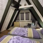 Schlafzimmer mit Dachschrägen, Bett, Sessel und TV. Fenster mit Jalousien und Herzanhänger.