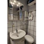 Badezimmer mit Waschbecken, Spiegelschrank und Toilette. Wandfliesen und Duschbereich sichtbar.