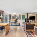 Living and dining area with wooden floor, sofa, dining table, and wood stove.