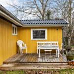 Yellow house with wooden terrace, white table and chairs, surrounded by trees.