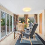 A room with two gray chairs, a wooden dresser, and large windows to the outside.