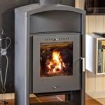 A wood-burning stove stands on tiled floor. To the left, a fireplace tool hangs.
