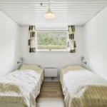 Two single beds, window with curtains, ceiling light, and clothes rack.