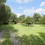 House with garden, terrace, and forest in background. Path leads to entrance.