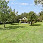 A yellow house with a terrace stands on a green lawn between trees.
