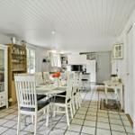 Dining area with table and chairs, kitchen with worktop and cabinets, white walls and floor tiles.