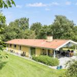A yellow house with terrace and garden. Surrounded by trees under blue sky.