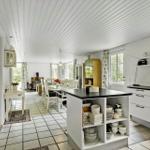 Kitchen with dining area, white cabinets, and black countertop. Windows and ceiling with wood paneling.
