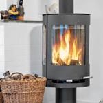 A wood-burning stove with burning logs, next to a basket of firewood and decorative figurines.