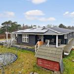 A dark blue vacation home with terrace, trampoline, and red shed in the grass.