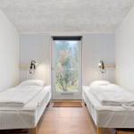 Two beds with white bedding face a glass door.