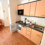 Küche mit Holzschränken, Spüle und Kühlschrank. Im Hintergrund ist Essbereich mit Tisch und Stühlen.