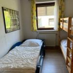 A room with a single bed and a wooden bunk bed. A picture hangs on the wall.